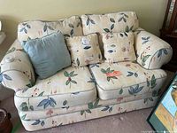 Front angle of 2-seater floral fabric sofa with three cushions: two floral patterned cushions and one solid blue cushion.