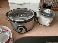 Slow cooker, rice cooker, and blender together with a partial view of red and white mugs.