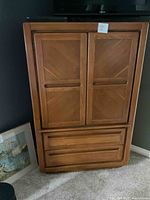Front view of closed wooden armoire cabinet with paneled doors and bottom drawers.