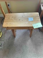 Front and slightly angled front view of a rustic wooden bench with light natural finish, showing the top, legs, and surface wear.