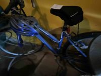 Blue women's cruiser bike with helmet on handlebars and black seat cover, partially visible in dimly lit area.