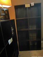 Front view of the full black bookcase showing its tall rectangular shape with square shelving compartments.