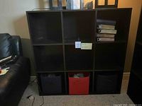 Front view of black bookcase showing nine empty cubed compartments with some fabric bins and stacked items on top right compartment.
