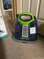 Front view of Bissell Little Green Pro Pet carpet cleaner in translucent blue and green colors with hose wrapped at base.