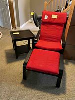 Red chair with ottoman and black side table arranged together on carpeted floor, showing the full set in one photo.