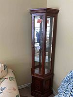 Front view of cherry wood corner curio cabinet with glass front panels and decorative top molding.