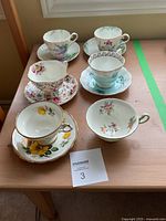 Top view of 6 floral fine china teacups on saucers arranged in two rows on wooden table shown from above