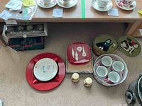 Wide shot showing assorted Christmas themed plates, mugs, platters including large red plate, character mugs, salt and pepper shakers.