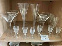 Full front view of 12 crystal glasses on a shelf including cordial liqueur glasses, champagne flutes and martini glasses
