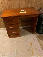 Full view of the wooden desk showing the three drawers on the left and open leg space on the right.