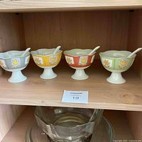 Front view of four floral dessert cups on pedestal bases with matching ceramic spoons, arranged on a wooden shelf.