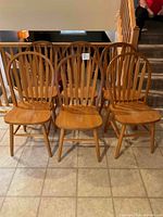 Front view of six matching oak dining chairs arranged in two rows of three, showing rounded slat backrest and wooden seats.