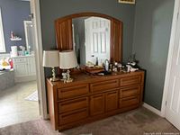 View of dresser and mirror with items on top, showing drawer configuration and wood finish.
