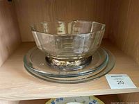 Clear glass pedestal bowl resting on the large glass serving platter, shelf background