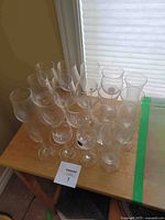 Top view showing 20 clear glass stemmed wine glasses of assorted shapes on a wooden table.