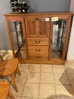 Front view of wooden kitchen buffet showing three central drawers with metal handles, a cabinet above, two side glass display cabinets with shelves inside, natural wood finish.