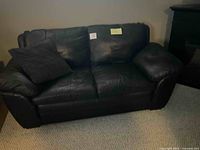 Photo showing front view of the black leather 2-seater couch with one matching cushion on the left side.