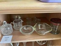Front view of the 7 pieces of crystal and glass on a wooden shelf, showing the sugar bowl, creamer, beaded edge bowl, star dish, and glass container with lid.