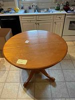 Photo of round oak dining table on tiled kitchen floor, showing tabletop and pedestal base.