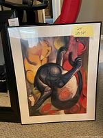 Framed print "Two Cats, Blue and Yellow" by Franz Marc leaning against a red chair, showing the artwork and black frame with a yellow size note attached.