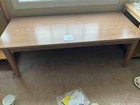 Top and leg view of light-colored solid wood rectangular coffee table in good condition, placed indoors on carpet.