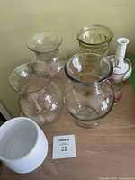 Photo showing five clear glass vases and two porcelain vases on a wooden surface.