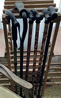 Photo showing six wooden canes with curved handles, in various colors and finishes, leaning on a drying rack.