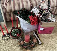 Wide shot showing assorted Christmas decorations including candles, floral stems, and Santa figurine in a box on carpet.