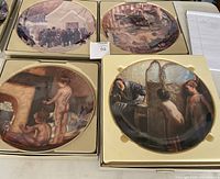 Four oval collector plates in original boxes showing artwork by A. Sherriff Scott and Paul Peel. Plates are arranged on a table with a lot number card visible.