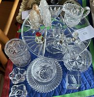 Overview of crystal and glassware items including pedestal cake plate, shakers, candle holders, creamers, bowls, plates, small pitcher, and a decorative flower figurine.