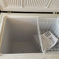 Open white Kenmore chest freezer showing clean interior with one wire basket on right side and user manual inside.