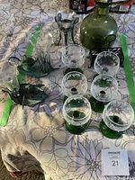 Full lot on floral tablecloth showing six green stemmed etched wine glasses, green glass decanter, two cast iron rabbits, and flower-shaped glass vases.