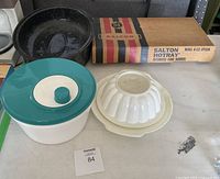 Wide view of the lot showing all four main items on table: roaster, salad spinner, Jello mold, and boxed food warmer.