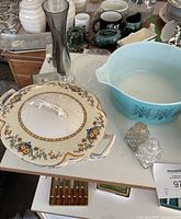 Photo showing two ornate floral-patterned ceramic serving bowls with lids, blue Pyrex casserole dish, and crystal salt and pepper shakers on a table.