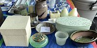 Overview of assorted pottery, keepsake boxes, candles, and small bowls arranged on blue fabric.