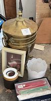 Brass container with lid, framed picture, two candle holders, and box of candles arranged on floor