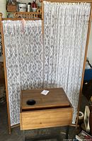 Full view of the Victorian privacy divider with three wooden panels covered in white lace fabric and the light walnut wood end table placed in front.