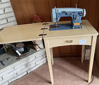 Side view of sewing machine mounted on the table with the extendable leaf open, showing the metal blue sewing machine and the cream table.
