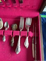 Close-up of forks, small fork, and specialty utensils in red felt-lined wooden box showing detailing of silver plated handles.