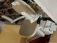 Close-up photo of one beige seat of the stair lift attached to white metal base and armrests with controls.