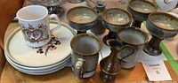 Photo showing 4 stoneware goblets, 4 plates with floral design, 2 cups, a commemorative cup and a small metal candlestick holder.