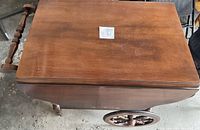 Top view of antique wooden tea cart with drop leaf closed, showing surface wear and wood grain.