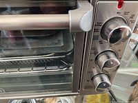 Close-up view of toaster oven door, handle, and control knobs showing temperature, function, and timer settings.