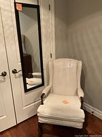 Off white wingback armchair with wooden legs, positioned in front of white doors, showing overall shape and upholstery pattern.