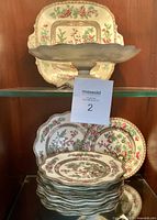 Front view of the serving platter and stacked decorative plates inside a glass cabinet, showing the Indian Tree floral pattern.