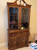 Front view of closed wooden antique china cabinet with glass paneled doors featuring decorative mullions, drawer and lower cabinet doors with brass handles.