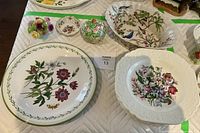 Set of collectible floral china pieces arranged on a quilted surface including a Studio Nova garden bloom plate and Lord Nelson floral pottery plate with a small Schumann Bavarian ceramic bowl.