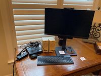 Overview photo showing Lenovo ThinkCentre Tiny-in-One monitor on stand with ThinkCentre Tiny PC, keyboard, mouse, speakers and cables on wooden table.