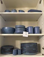 Overview of middle and bottom cabinet shelves showing serving bowl, stacked soup bowls, mugs, dinner and salad plates, salt & pepper shakers