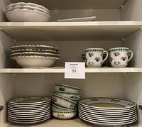 Cabinet shelf with stacks of salad plates, bowls and dinner plates at bottom, and soup bowls with mugs above.